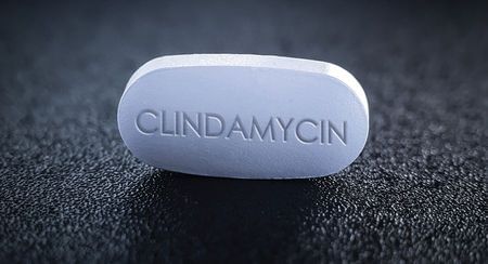 A single white rectangular pill with rounded edges and CLINDAMYCIN written in capitals on it