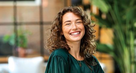 A smiling woman with curly hair in a dark forest green top