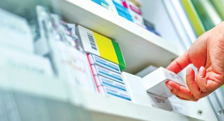 A hand taking a packet of medicine off a pharmacy shelf
