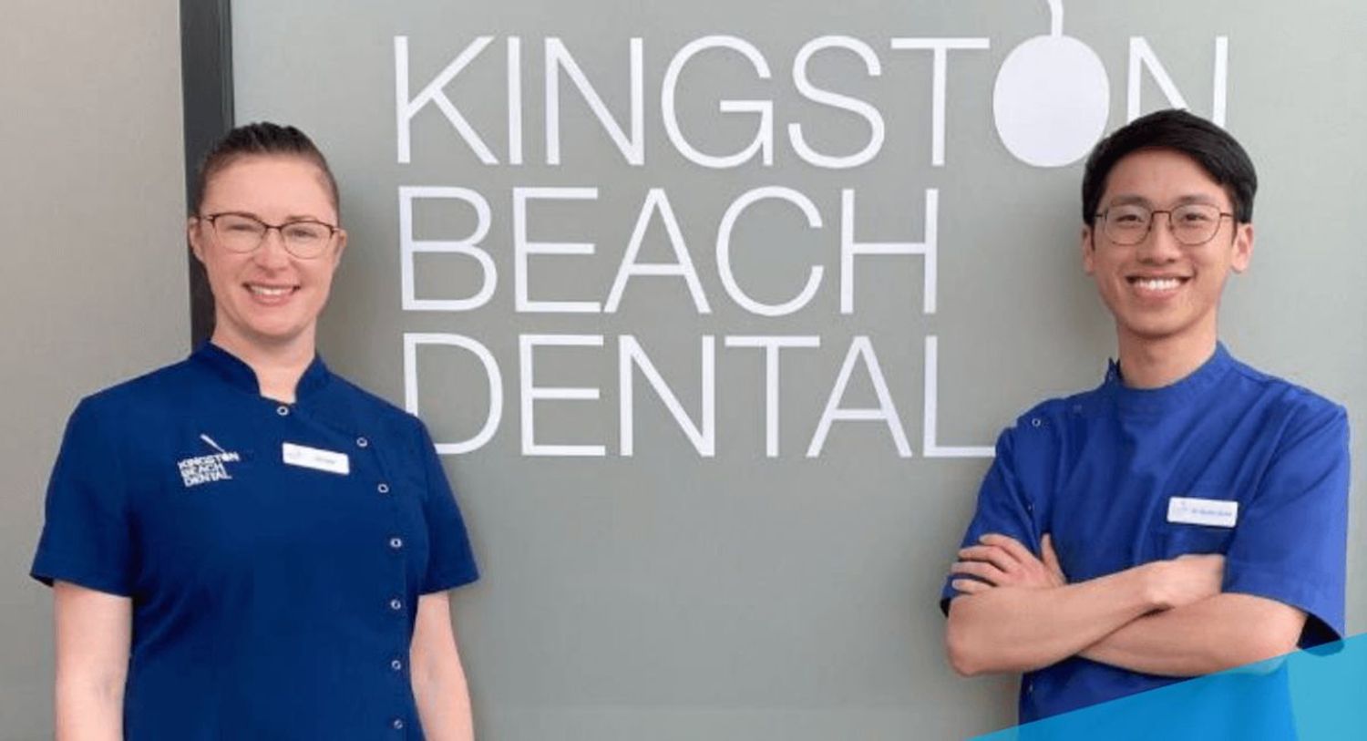 Smiling man and woman in blue dental scrubs in front of a practice sign