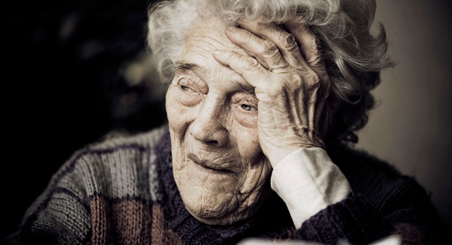 Old unhappy-looking wrinkled woman with head on hand