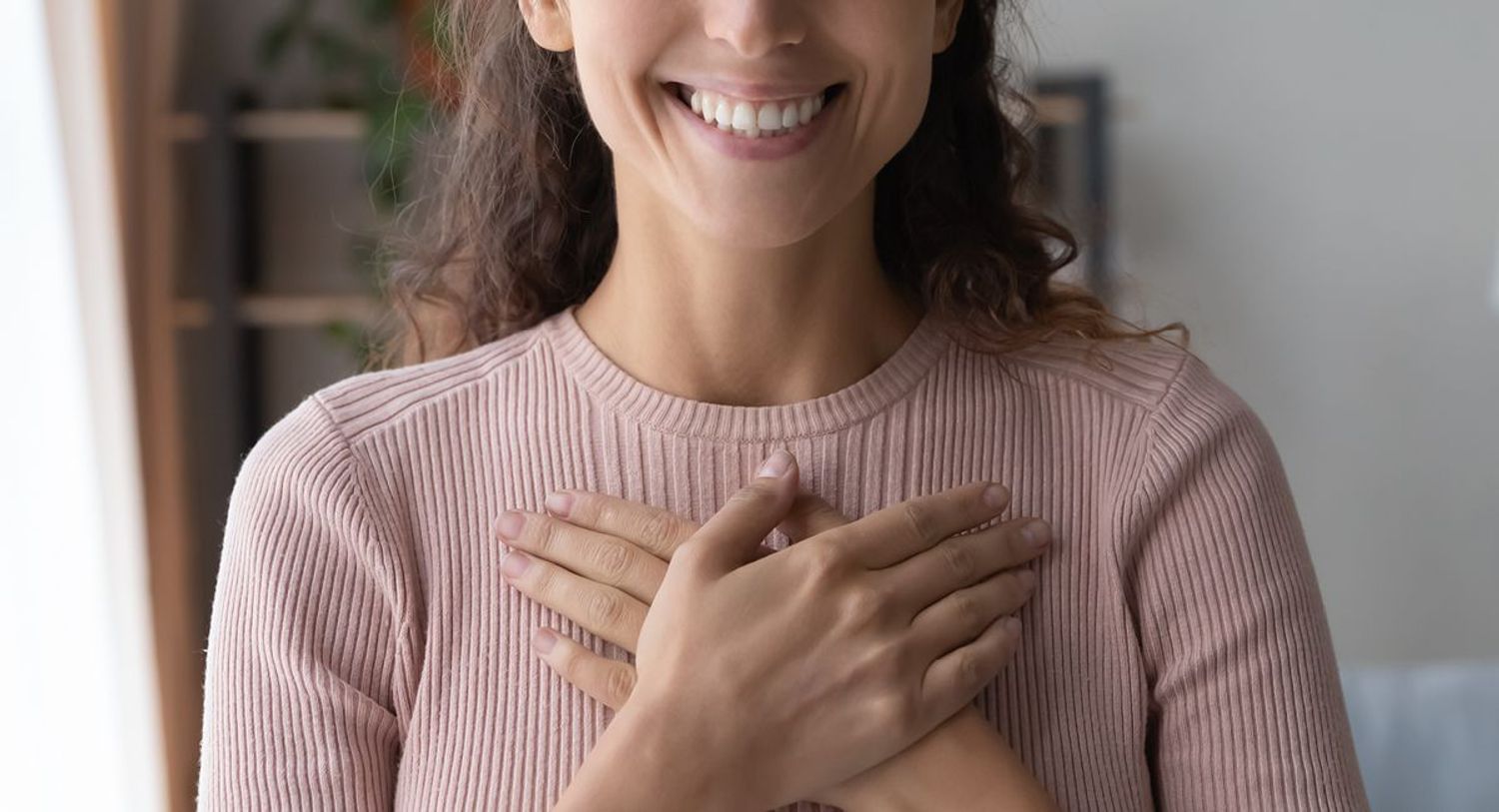 Woman in a pink jumper with hands across her heart