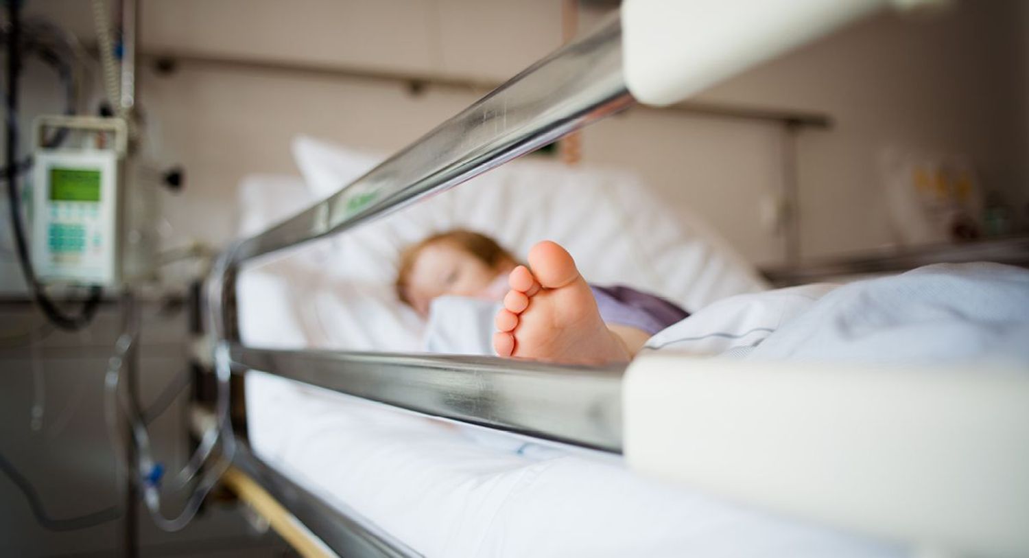 A child lying in a hospital bed out of focus with sheet over them