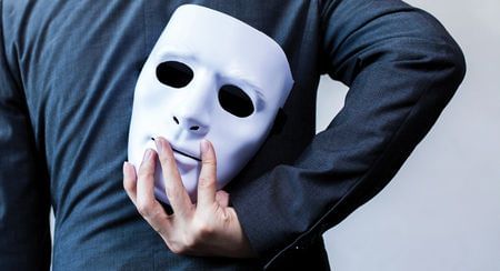 A man in a blue top holding a white mask behind his back