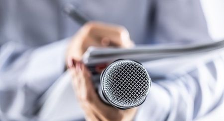 Journalist writing notes on a pad while microphone rests on their leg