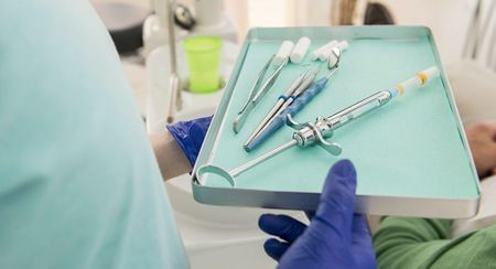 Sharps on a green background on a tray being held by practice staff