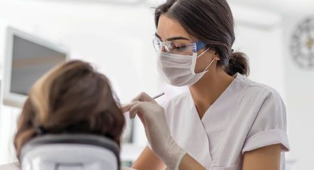 A masked female dentist working on a patient (can only see the back of the patient's head)