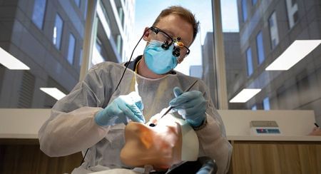 A dentist with a loupe on working on a model of a person's mouth