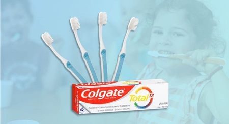 Four Colgate toothbrushes arranged in a fan over a tube of Colgate toothpaste