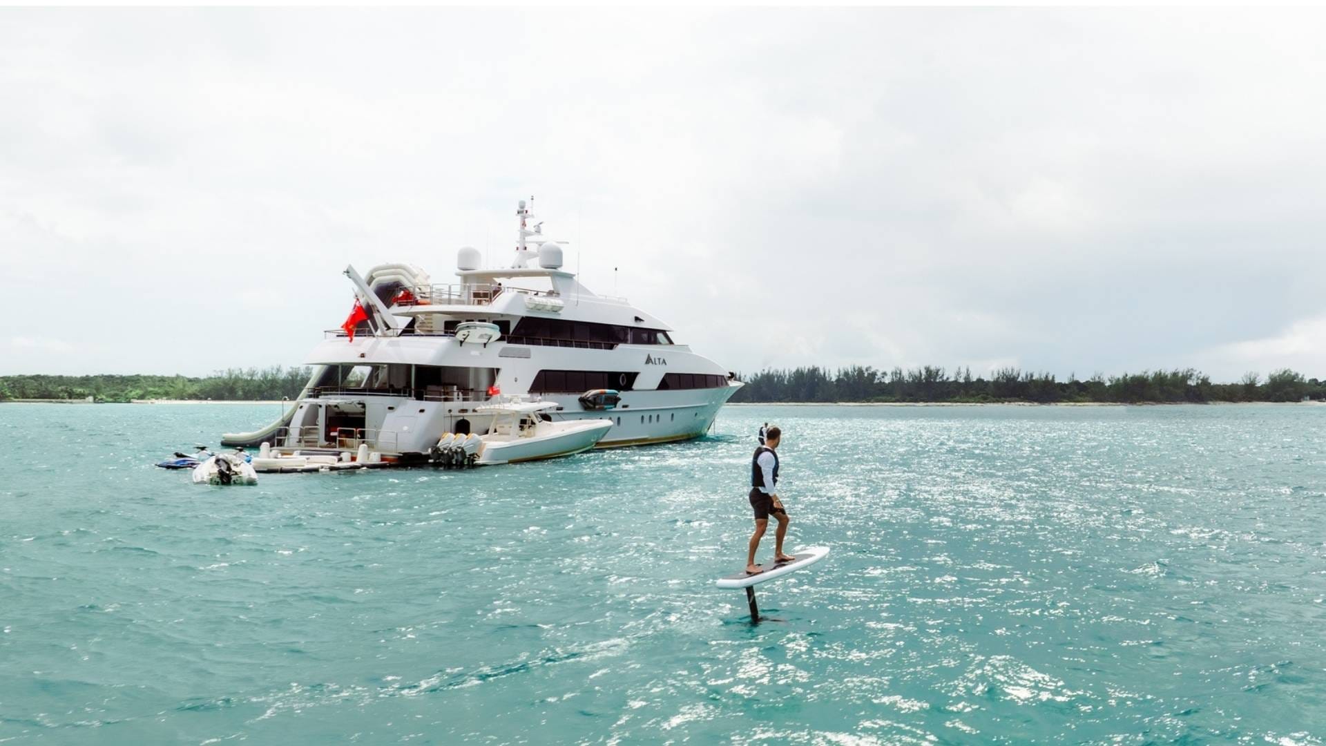 man on a wakeboard sailing next to a yacht