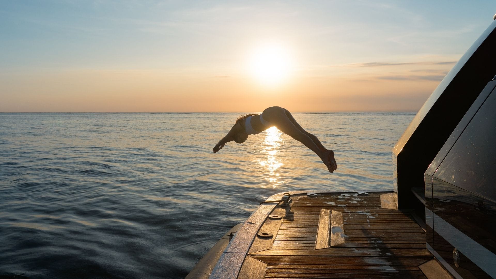 a young female diving into the see from yacht's swim platform during sunset