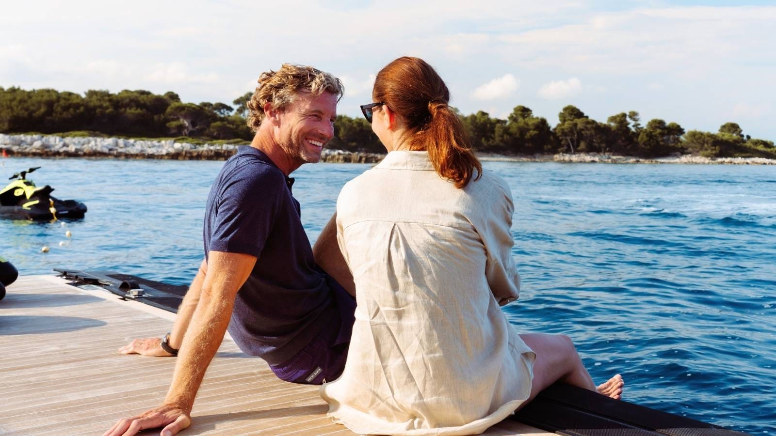 a man and a woman sitting on a dock and chatting