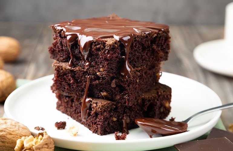 brownie com nozes e calda de chocolate ao lado de uma colher com chocolate e em cima de um prato branco.