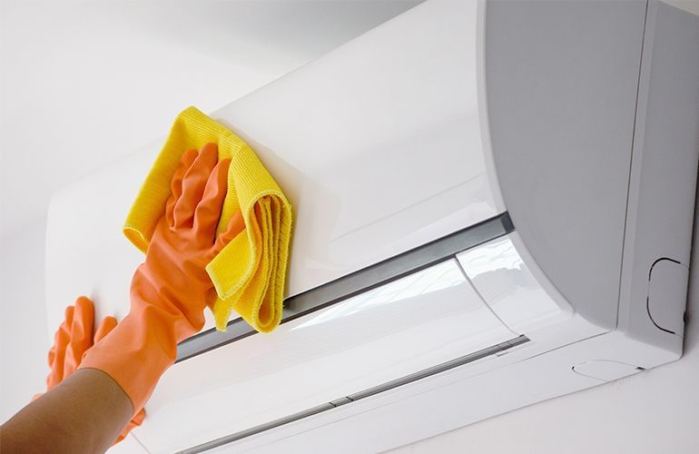 Pessoa fazendo a limpeza externa do ar-condicionado usando luvas e pano úmido com detergente neutro