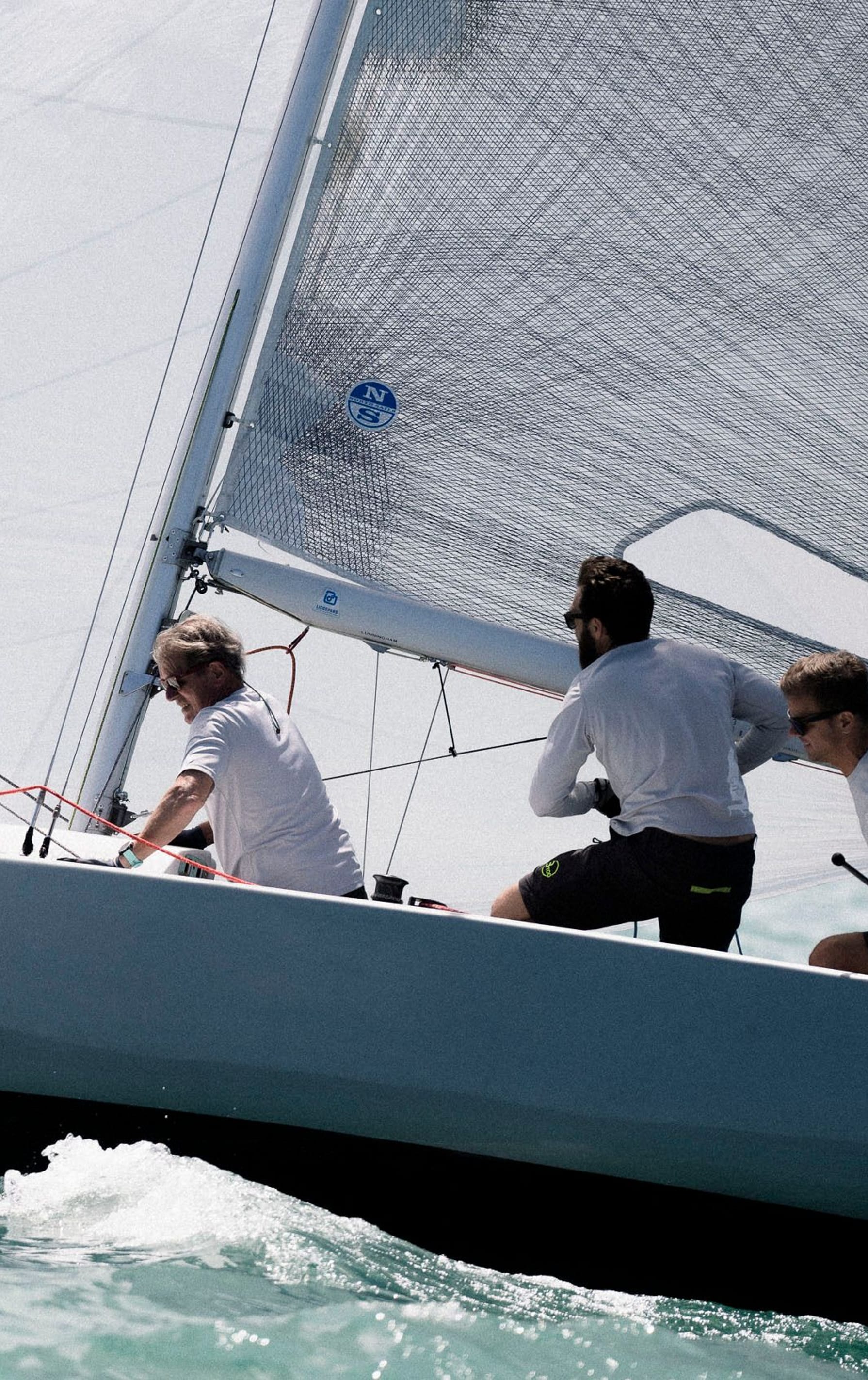 Drei Crewmitglieder in weißen Shirts konzentriert am Segeln auf einem Segelboot mit der Nummer 'SUI 4352' auf einem türkisfarbenen Gewässer. Besuchen Sie esseboats.ch für weitere Informationen.