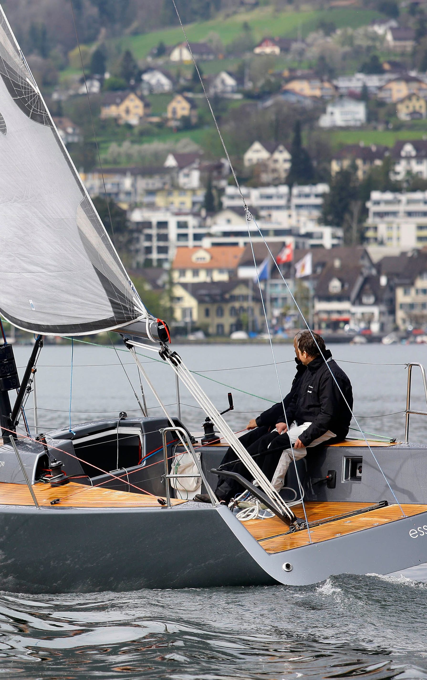 STU0117: Ein Segelboot der Marke 'Esse' mit schwarzen Segeln segelt majestätisch auf einem ruhigen See, umgeben von grünen Hügeln. Besuchen Sie esseboats.ch für weitere Informationen.