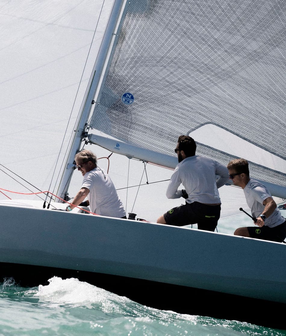 Drei Crewmitglieder in weißen Shirts konzentriert am Segeln auf einem Segelboot mit der Nummer 'SUI 4352' auf einem türkisfarbenen Gewässer. Besuchen Sie esseboats.ch für weitere Informationen.