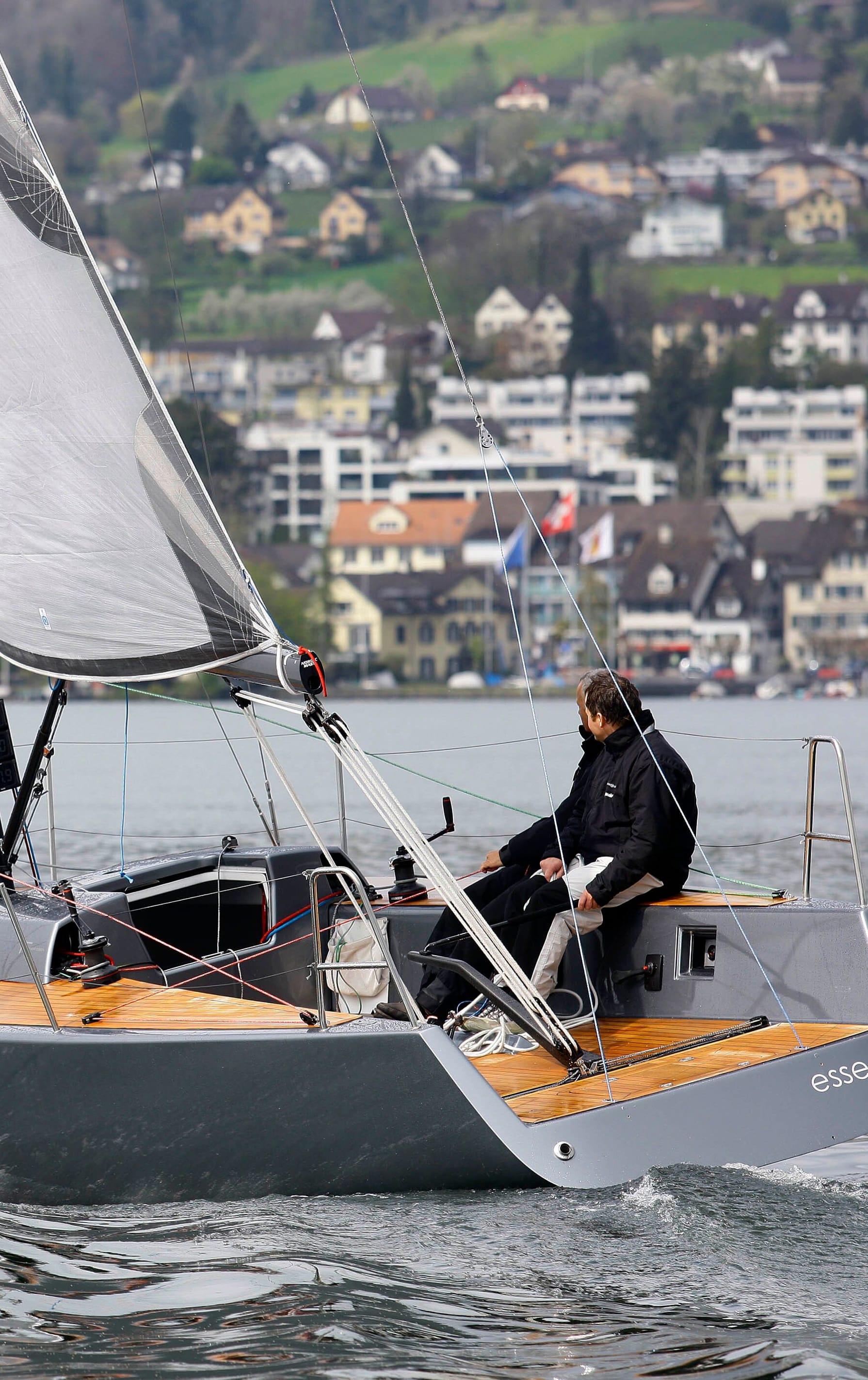STU0117: Ein Segelboot der Marke 'Esse' mit schwarzen Segeln segelt majestätisch auf einem ruhigen See, umgeben von grünen Hügeln. Besuchen Sie esseboats.ch für weitere Informationen.
