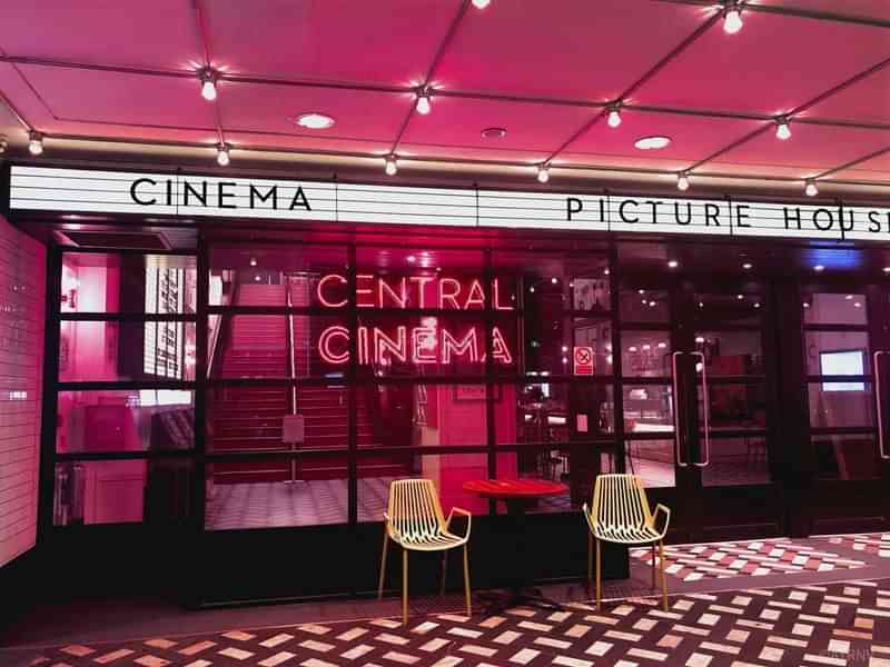 Modern movie theater entrance with neon lights and marquee signage.