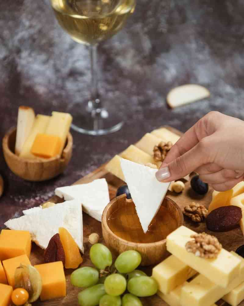 Kaasplank met verschillende kazen, noten, fruit en een glas wijn.