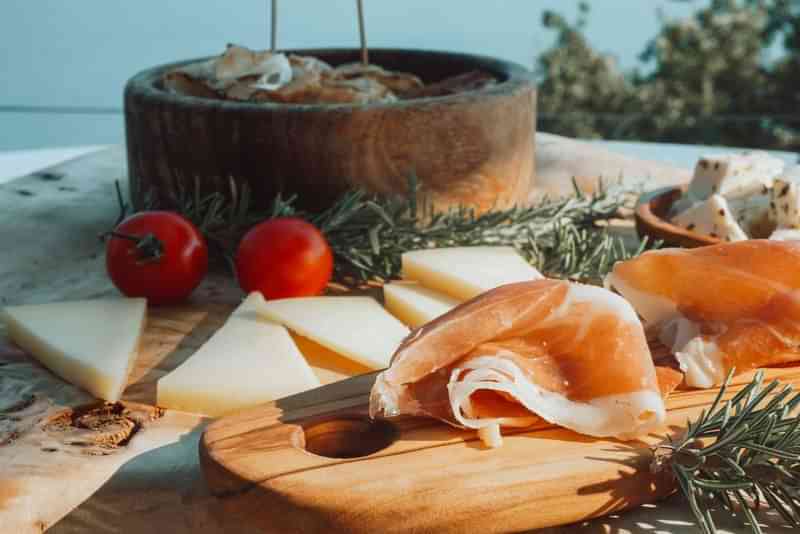 Kaas, ham, tomaten en kruiden op een houten plank.