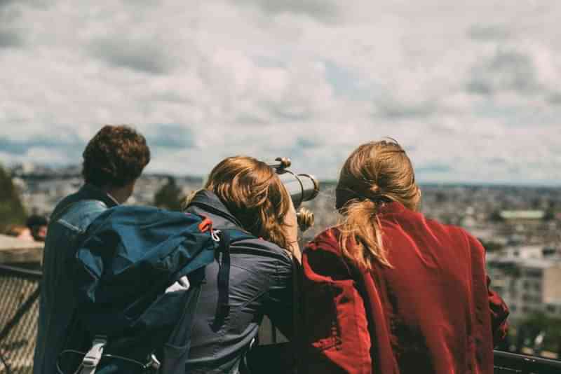 Tourists overlooking a cityscape through a telescope, exploring new destinations.