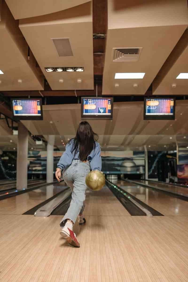 Woman bowling at a bowling alley, large screens display scores.