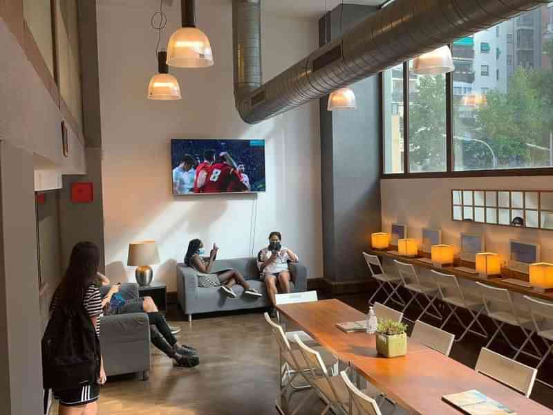 People relaxing in a common area with a TV and workspaces.