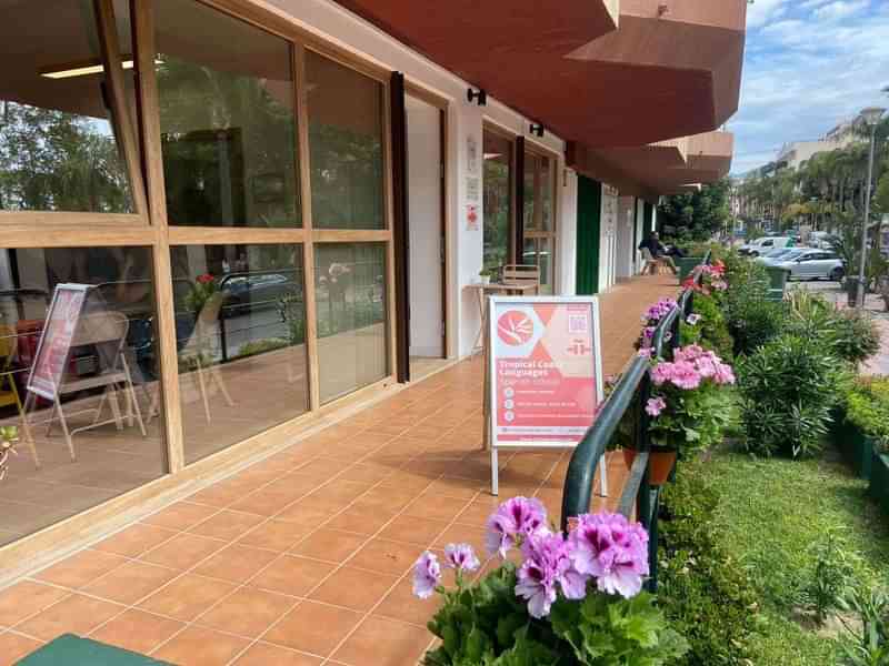 Taalinstituut met bord, zonnig outdoor terras, bloemen en groene omgeving.