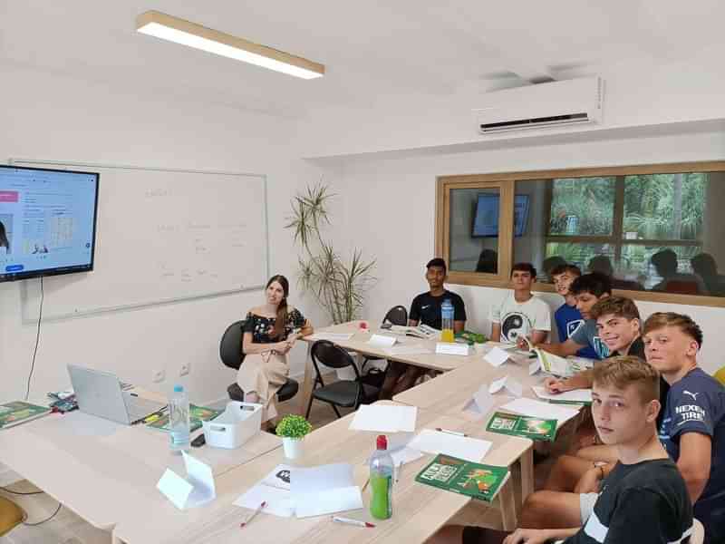 Taalstudenten in klaslokaal, luisteren naar leraar, bekijken scherm, leren samen.