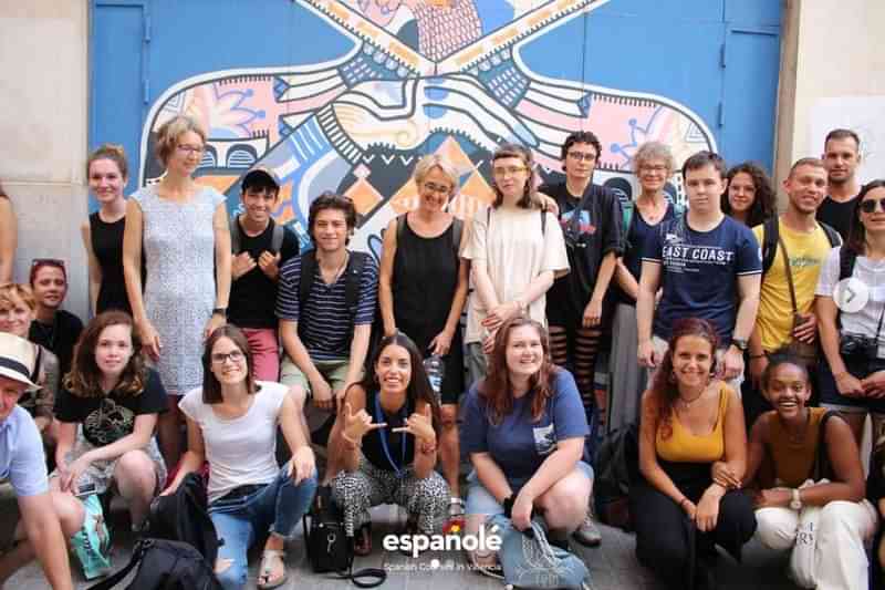 Een groep internationale studenten poseert voor een kleurrijke muurschildering.