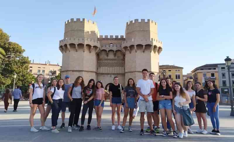 Groep studenten voor historisch gebouw tijdens taalreis, zonnige dag.