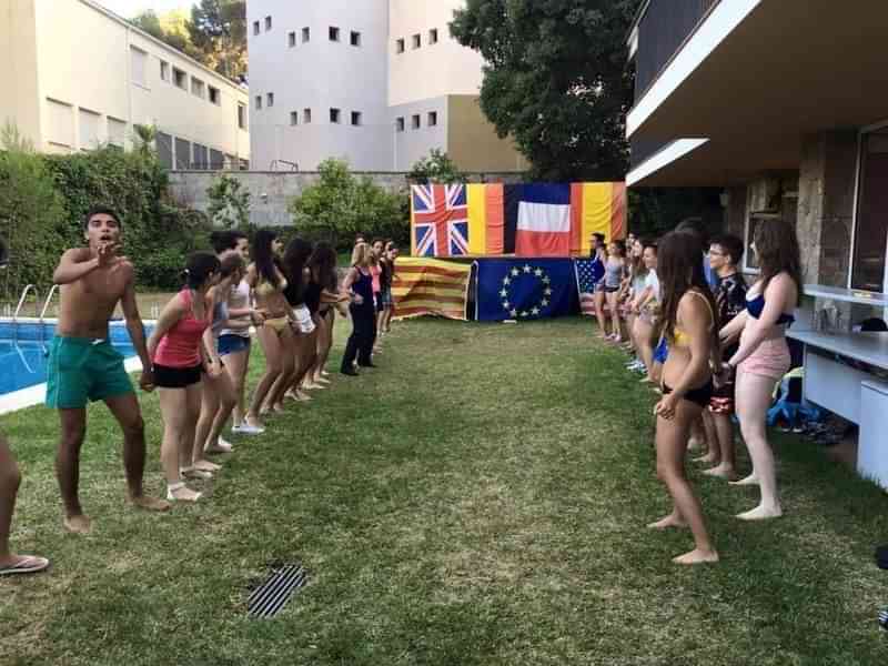 Groep jongeren bij zwembad, vlaggen van verschillende landen, mogelijk taalkamp.