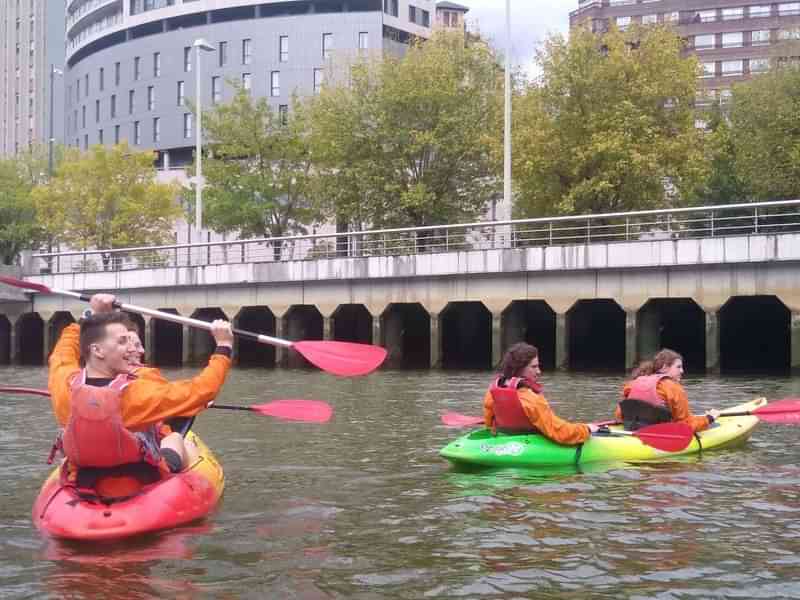 Mensen kajakken in een rivier in een stedelijke omgeving.