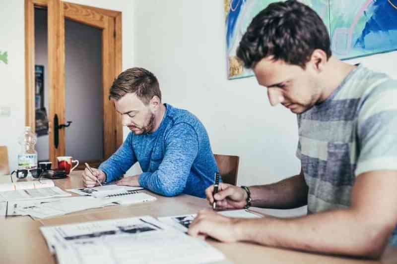 Twee mannen studeren samen taal met lesmateriaal op de tafel.