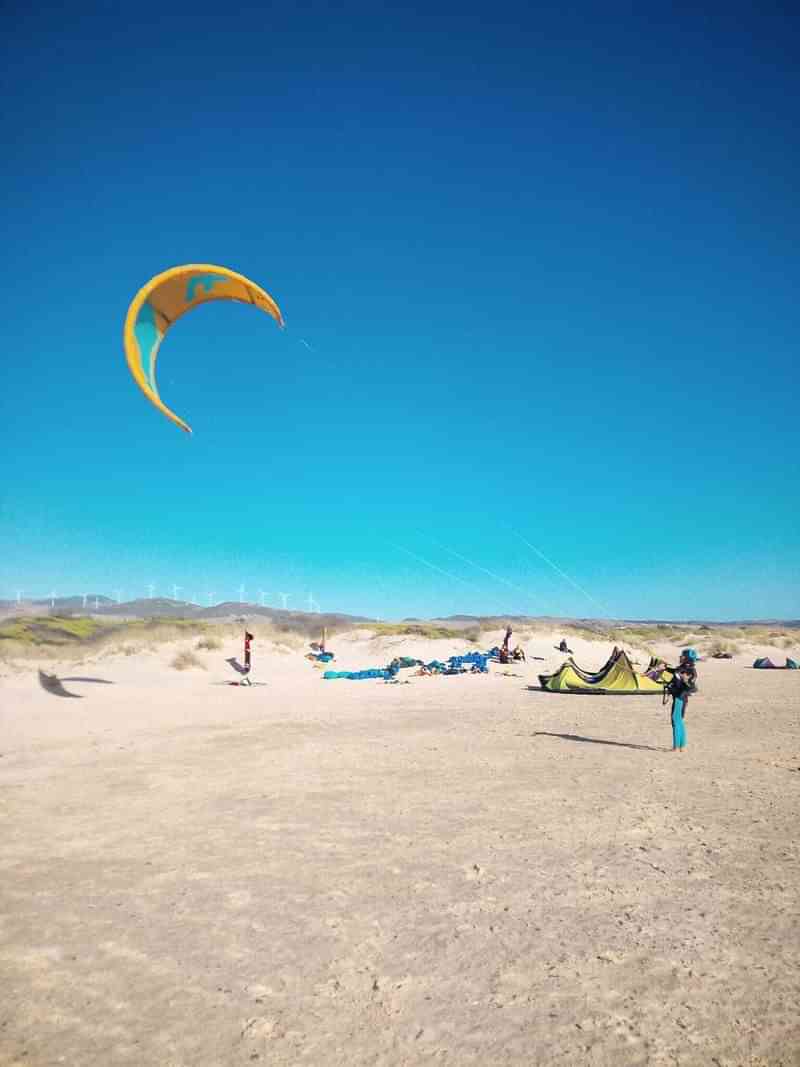 Kitesurfen op een zonnig strand, omgeven door zandduinen.