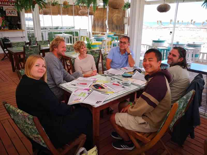 Groep mensen aan tafel tijdens taalles in strandcafé.