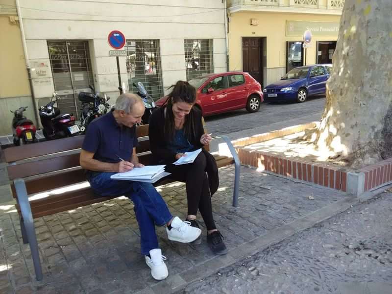 Two people studying language material together on an outdoor bench.