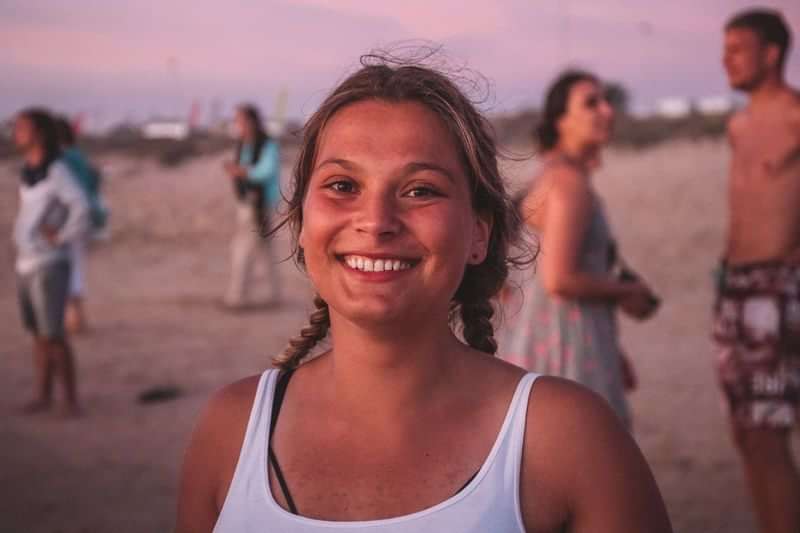 Een vrouw glimlacht op het strand tijdens een culturele uitwisseling.