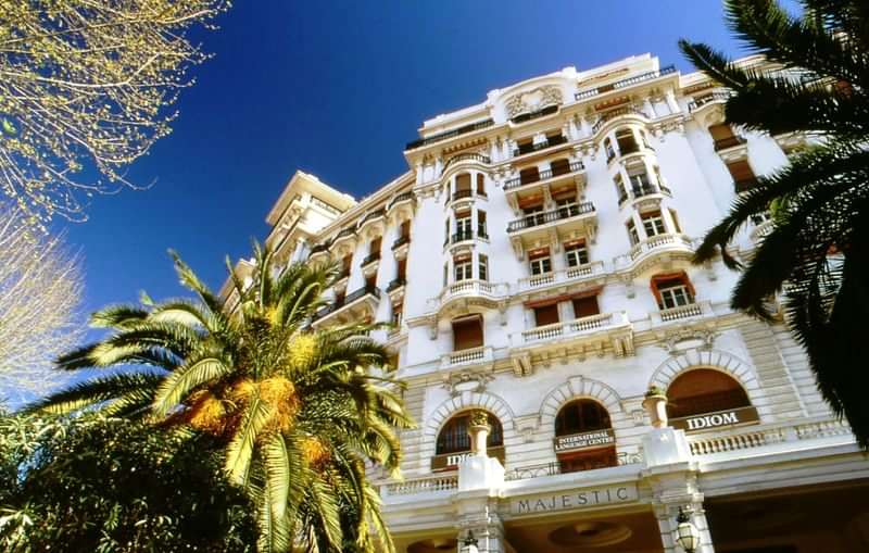 Elegant hotel facade with balconies, palm trees; ideal for language immersion stay.