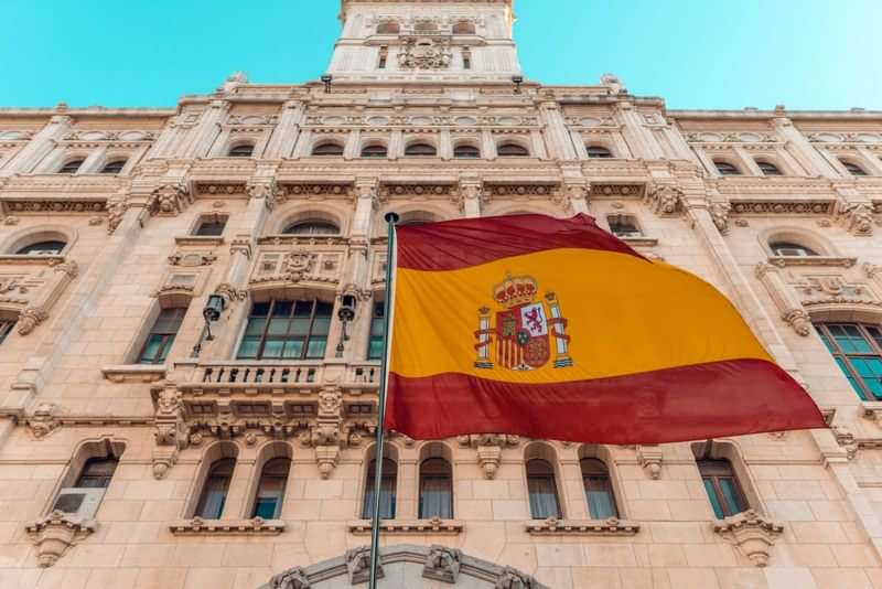 Spanish flag in front of a historical building, ideal for language immersion.