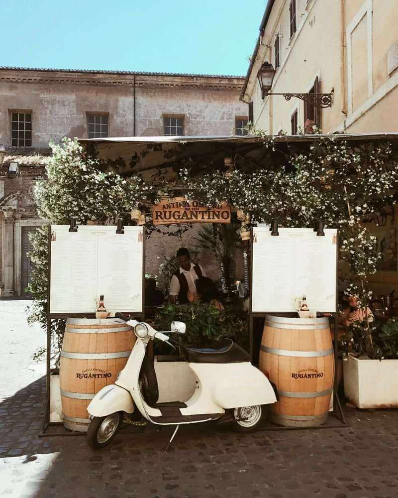 Quaint Italian café with menus, a scooter, and wine barrels.