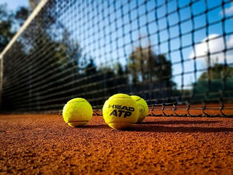 Tennisbaan met tennisballen, ideaal voor sportieve taalreizen in Nederland.