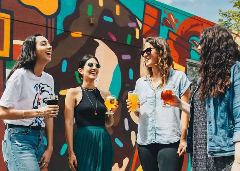 Groep vrienden geniet van drankjes, buiten bij een kleurrijke muurschildering.