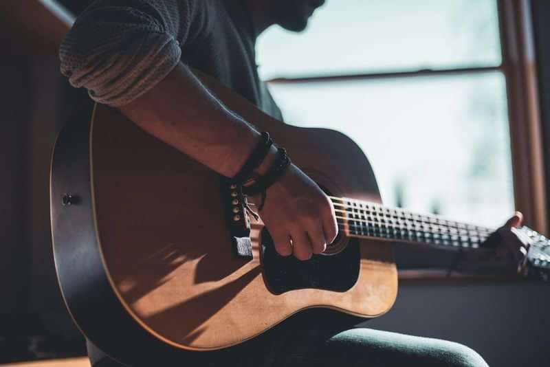 Person playing guitar, enhancing language skills through travel and music.