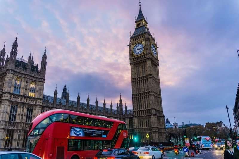 Big Ben at sunset with red London buses and traffic.