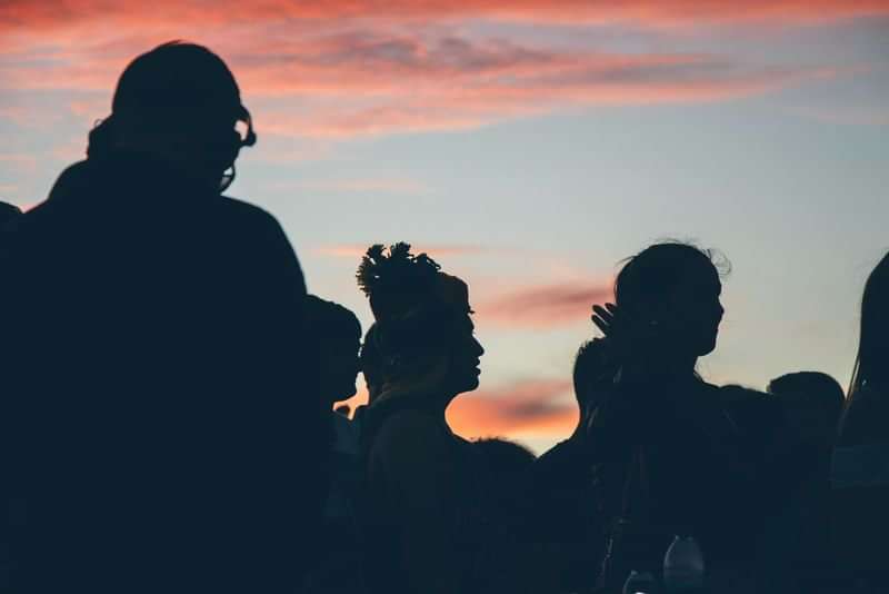 Groep mensen silhouetten bij zonsondergang, culturele taalreis-ervaring.