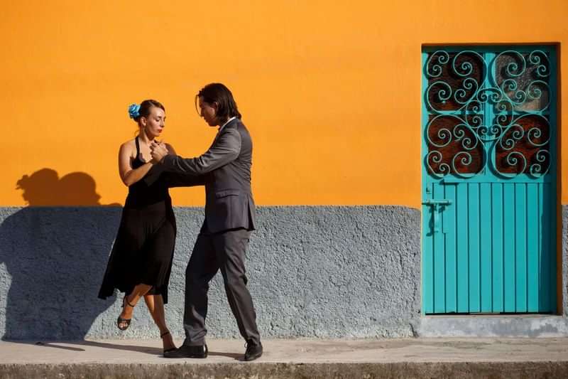 Couple dancing tango outside, vibrant orange wall, teal ornate door.