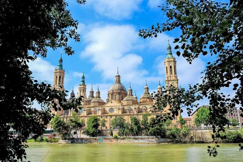 Basilica viewed through trees, located in Zaragoza, Spain, along a river.
