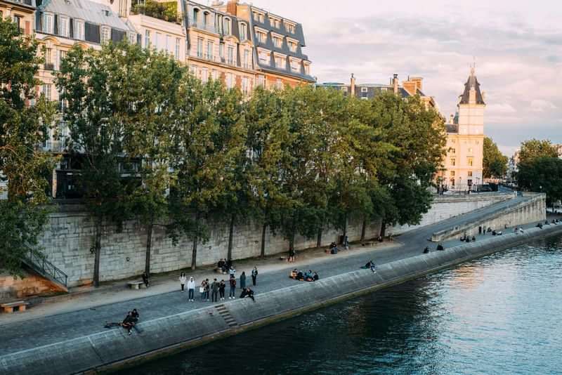 People by a riverside in a European city, possibly Paris.